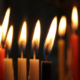 A closeup photo of nine lit candles in the darkness.