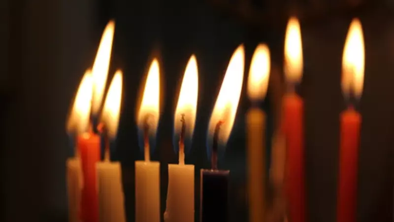 A closeup photo of nine lit candles in the darkness.
