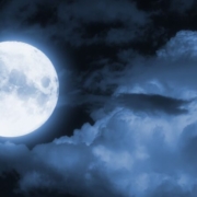 A full moon in a partly cloudy night sky.