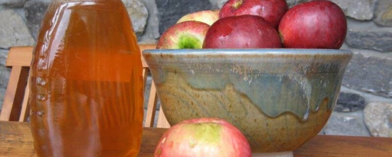 A jar of honey next to a bowl of red apples.